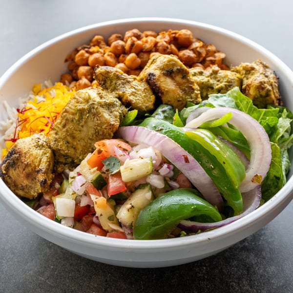 A Mediterranean bowl from Kabob Korner with chicken, chickpeas, rice, and fresh salad.