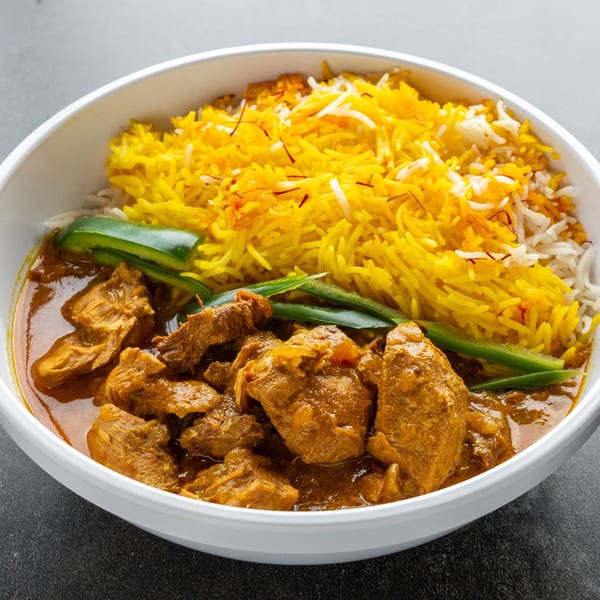 A white bowl filled with chicken curry, yellow saffron rice, and green peppers from Kabob Korner.