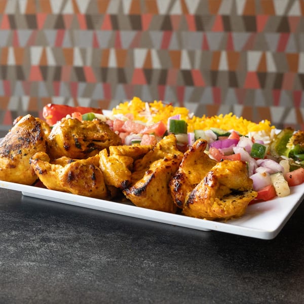 Grilled chicken kabobs with yellow rice and a fresh vegetable salad on a white platter.