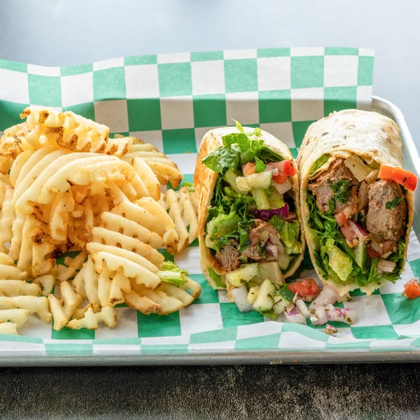 Two Mediterranean kabob wraps with fresh vegetables and meat, alongside a pile of waffle fries.