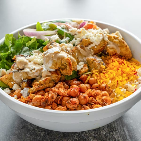A Mediterranean bowl with chicken, chickpeas, rice, lettuce, red onion, and feta cheese.